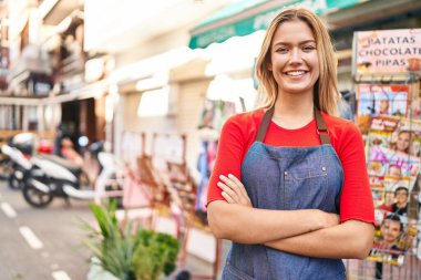 Young hispanic woman shop assistant standing with arms crossed gesture at street