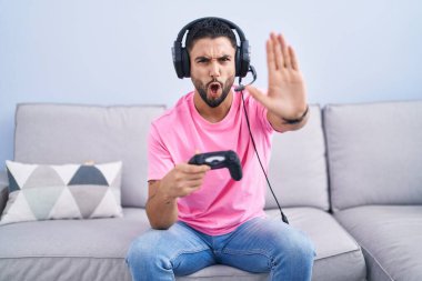 İspanyol genç adam video oyunu oynuyordu. Kanepede oturuyordu. El hareketlerini durduruyordu. 