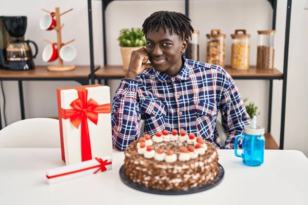 アフリカの男ですドレッドロックお誕生日を祝います大きなチョコレートケーキを保持します深刻な顔を考えます質問について手であご 混乱のアイデアについて思慮深い — ストック写真