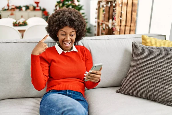 머리가아 프로인 아프리카계 스마트폰을 이용해 소파에 크리스마스 트리는 손가락으로 행복하게 — 스톡 사진