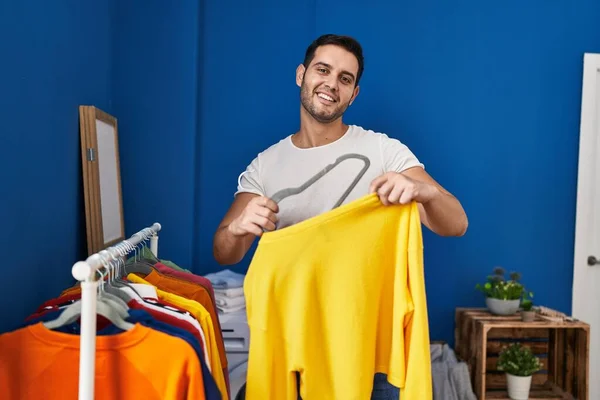 Young hispanic man putting clothes on clothes rack at laundry room