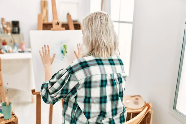 Young artist student girl on back view painting canvas with painted hands at art studio.