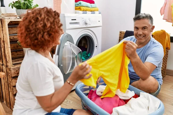 Middle age man and woman couple holding t shirt washing clothes at laundry