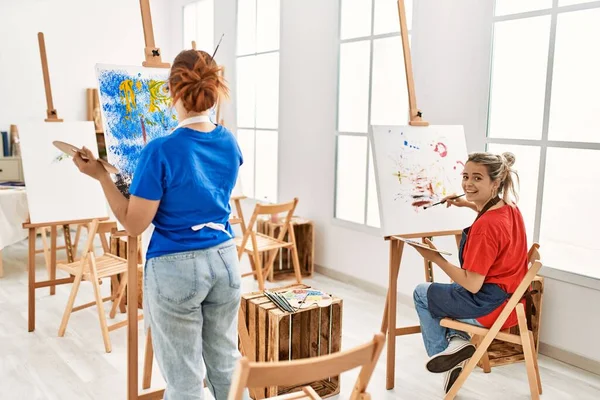 Two artist student women smiling happy painting at art school.