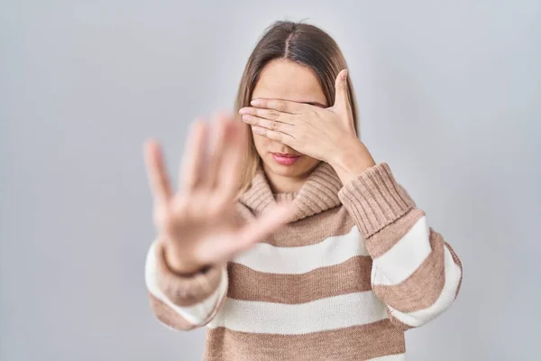 Young blonde woman wearing turtleneck sweater over isolated background covering eyes with hands and doing stop gesture with sad and fear expression. embarrassed and negative concept.