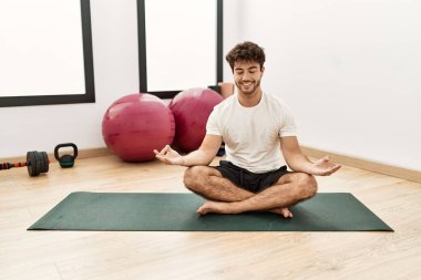 Genç İspanyol adam gülümsüyor spor merkezinde yoga antrenmanı yapıyor.