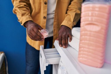 Genç Afrikalı Amerikalı adam gülümsüyor Çamaşır odasında çamaşır makinesine deterjan döküyor