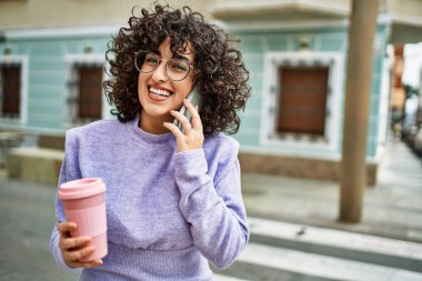 Orta Doğulu genç bir kadın gülümsüyor. Akıllı telefondan konuşuyor.