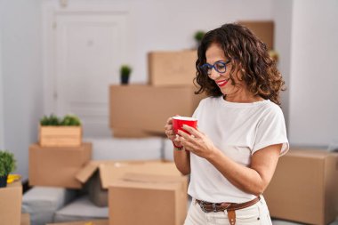 Middle age hispanic woman smiling happy drinking a cup of coffee at new home