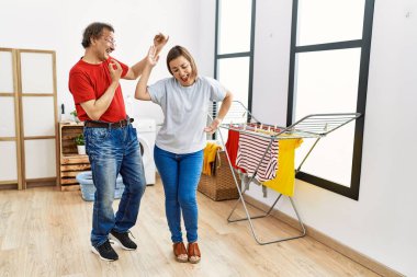 Orta yaşlı erkek ve kadın çamaşırhanede çamaşır makinesini beklerken dans ediyorlar.