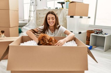 Paketteki köpeği tutan genç İspanyol kadın yeni evinde yerde oturuyor.
