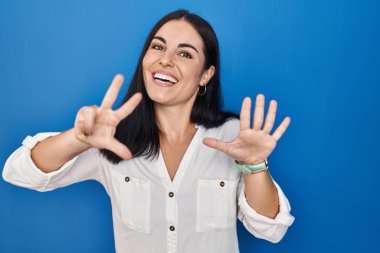 Mavi arka planda dikilen genç İspanyol kadın sekiz numaralı parmaklarını gösterip işaret ederken kendinden emin ve mutlu gülümsüyor.. 
