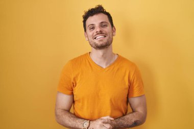 Sarı arka planda duran genç İspanyol adam ellerini kavuşturup gülümseyerek gevşemiş ve neşeliydi. Başarı ve iyimserlik 