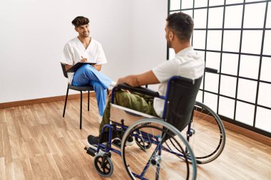 Tekerlekli sandalyede oturan iki İspanyol erkek ve hasta klinikte rehabilitasyon seansı yapıyorlar.