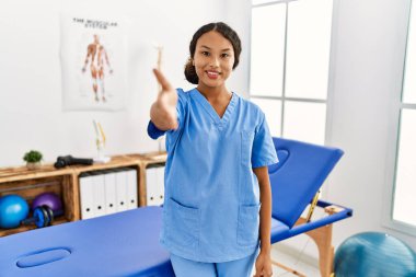 Ağrı kesici kliniğindeki güzel İspanyol fizyoterapist kadın selamlama ve hoş geldin demek için gülümseyerek tokalaşıyor. başarılı iş. 