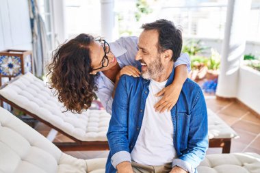 Orta yaşlı İspanyol çift gülümsüyor. Birbirlerine sarılıyorlar. Terasta hamakta oturuyorlar.