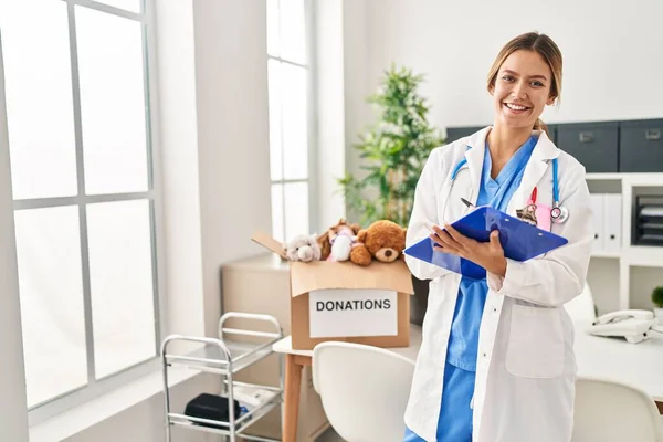 Young Hispanic Woman Wearing Doctor Uniform Writing Report Donations Toys — Foto de Stock
