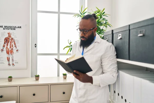 Young African American Man Wearing Doctor Uniform Reading Book Clinic — Fotografia de Stock