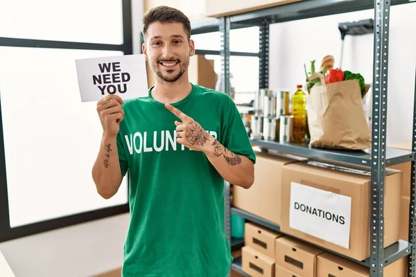 Joven Hombre Hispano Con Camiseta Voluntaria Sosteniendo Necesitamos Bandera Sonriendo — Foto de Stock