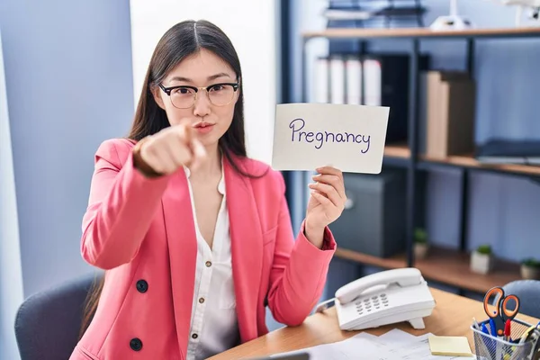 在办公室工作的中国年轻女子拿着怀孕标志 用手指着相机和你 自信地摆出一副严肃的样子 — 图库照片