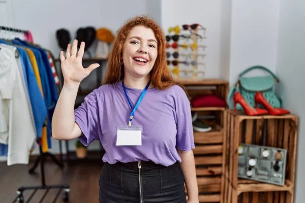 Young redhead woman working as manager at retail boutique showing and pointing up with fingers number five while smiling confident and happy.