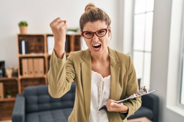 Danışmanlık ofisinde çalışan genç bir kadın öfkeyle bağırırken kızgın ve öfkeli bir şekilde yumruğunu kaldırıyor. öfke ve agresif konsept. 