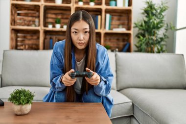Genç Çinli kız evdeki kanepede oturmuş video oyunu oynuyor..