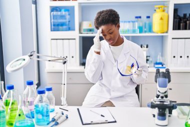 African american woman wearing scientist uniform stressed working at laboratory