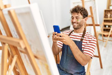 Young hispanic man make photo to draw using smartphone at art studio