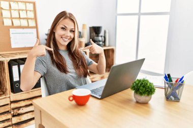 Young brunette woman working at the office with laptop looking confident with smile on face, pointing oneself with fingers proud and happy. 