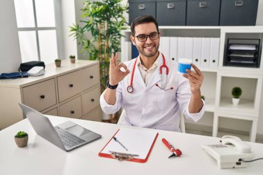 Sakallı, pamuklu sakallı genç İspanyol doktor parmaklarıyla imza atıyor, gülümseyerek mükemmel bir sembol oluşturuyor. 