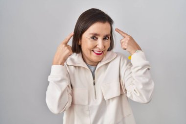 Middle age hispanic woman standing over isolated background smiling pointing to head with both hands finger, great idea or thought, good memory 