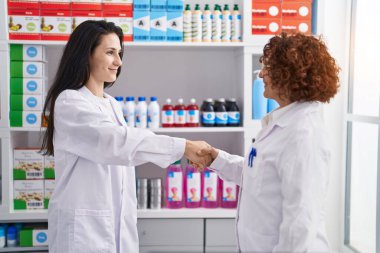 Eczanede kendine güvenen iki kadın eczacı el sıkışıyor.