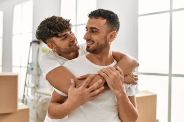 Two hispanic men couple smiling confident hugging each other standing at new home