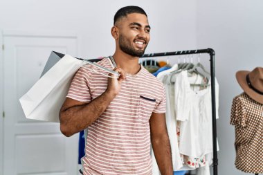 Giysi dükkanında alışveriş torbaları tutan genç bir Arap.