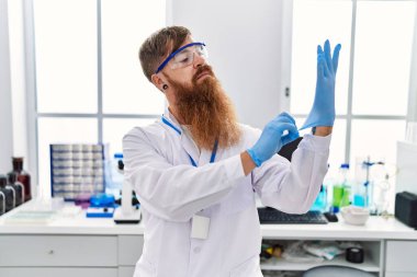 Laboratuvarda eldiven giyen, bilim adamı üniforması giyen genç bir kızıl.