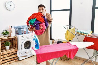 Çamaşırlarını ütülemeye hazır genç yakışıklı bir adam kamerayı işaret ediyor ve sen kendine güvenen ciddi bir hareket yapıyorsun. 