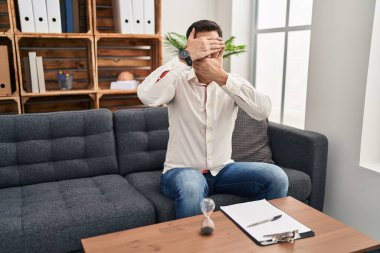 Danışma ofisinde sakallı, ağzı ve gözlerini kapayan, şaşırmış ve şok olmuş genç İspanyol bir adam. duygu gizleme 