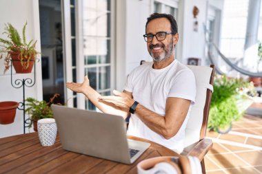 Middle age man using computer laptop at home inviting to enter smiling natural with open hand 