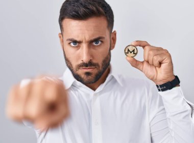 Monero kripto para taşıyan yakışıklı İspanyol adam kamerayı ve seni işaret ediyor. Kendine güvenen, ciddi bir hareket. 
