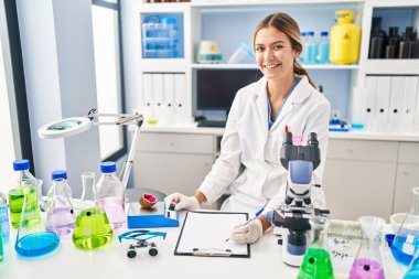 Young hispanic woman scientist weighing gemstone writing report at laboratory