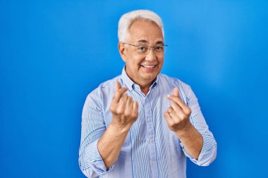 Hispanic senior man wearing glasses doing money gesture with hands, asking for salary payment, millionaire business 