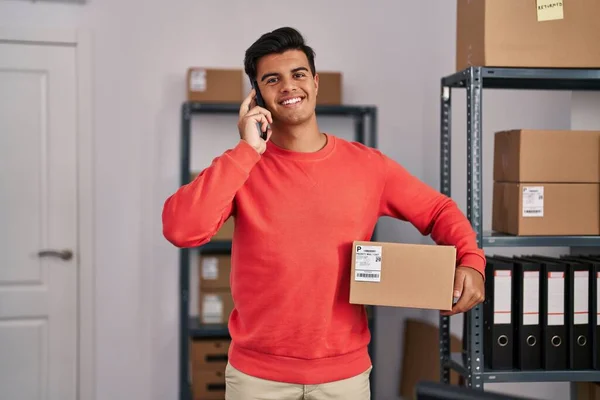 Young Hispanic Man Ecommerce Business Worker Talking Smartphone Holding Package — стоковое фото