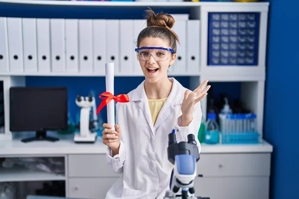 Teenager Girl Working Scientist Laboratory Holding Degree Celebrating Victory Happy — Stockfoto