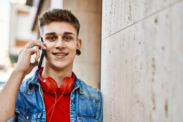Joven Chico Caucásico Sonriendo Con Teléfono Inteligente Apoyado Pared —  Fotos de Stock