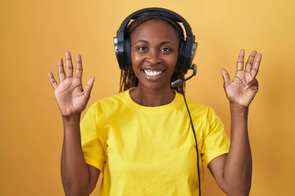 African american woman listening to music using headphones showing and pointing up with fingers number nine while smiling confident and happy.