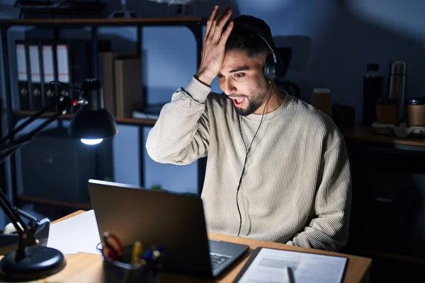 Young handsome man working using computer laptop at night surprised with hand on head for mistake, remember error. forgot, bad memory concept.