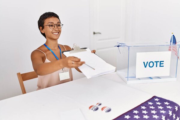 Молодая латиноамериканка улыбается уверенно держась контрольного списка, работая в колледже выборщиков