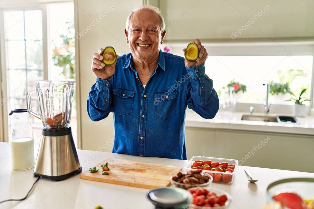 Senior man smiling confident holding two middles avocado at kitchen
