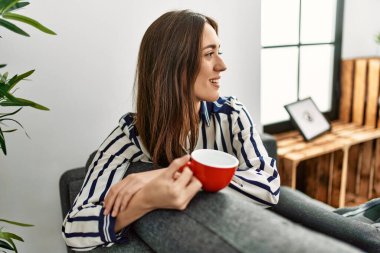 Genç İspanyol kadın evdeki kanepede kahve içiyor.